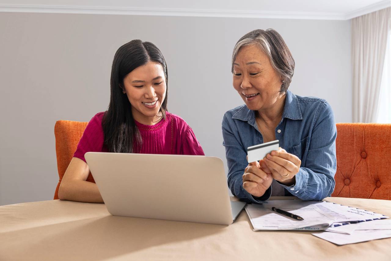 Adult daughter and her mother research on a laptop at a dining room table
